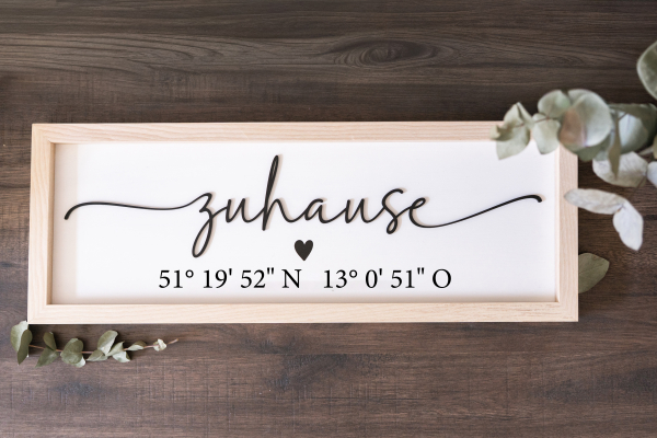 Holzschild „Zuhause“ mit schwarzen 3D-Acryl-Schriftzug und personalisierten Koordinaten im UV-Druck – Eschenholzrahmen, weißer Hintergrund